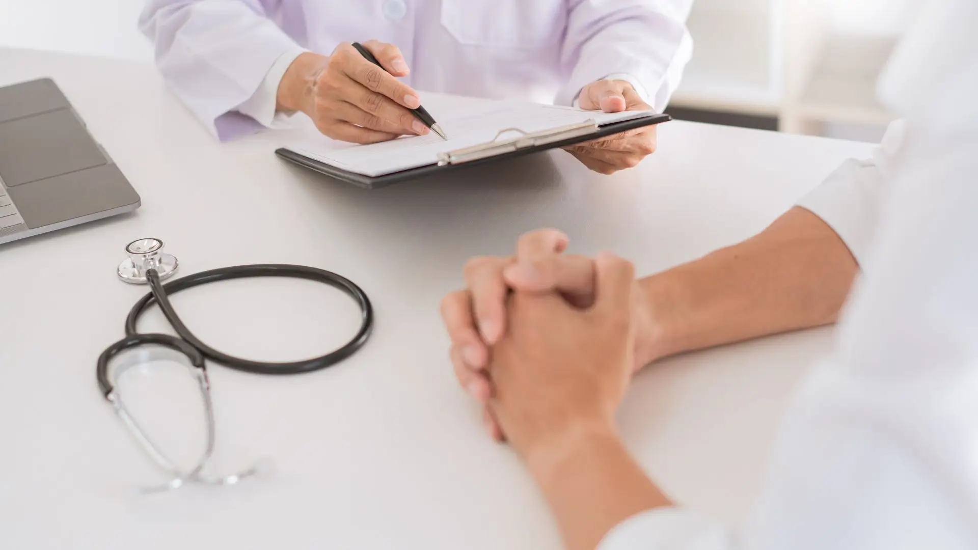 A doctor is talking to a patient in front of a laptop